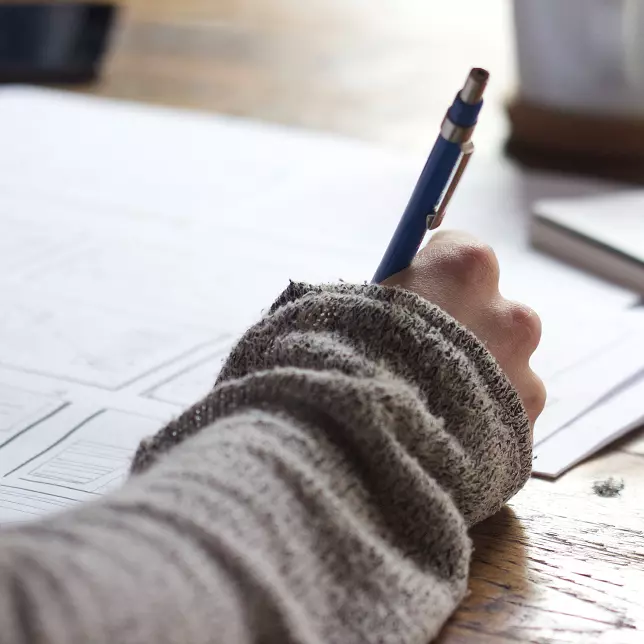 Picture of a person studying with a pen, notepad, and book.